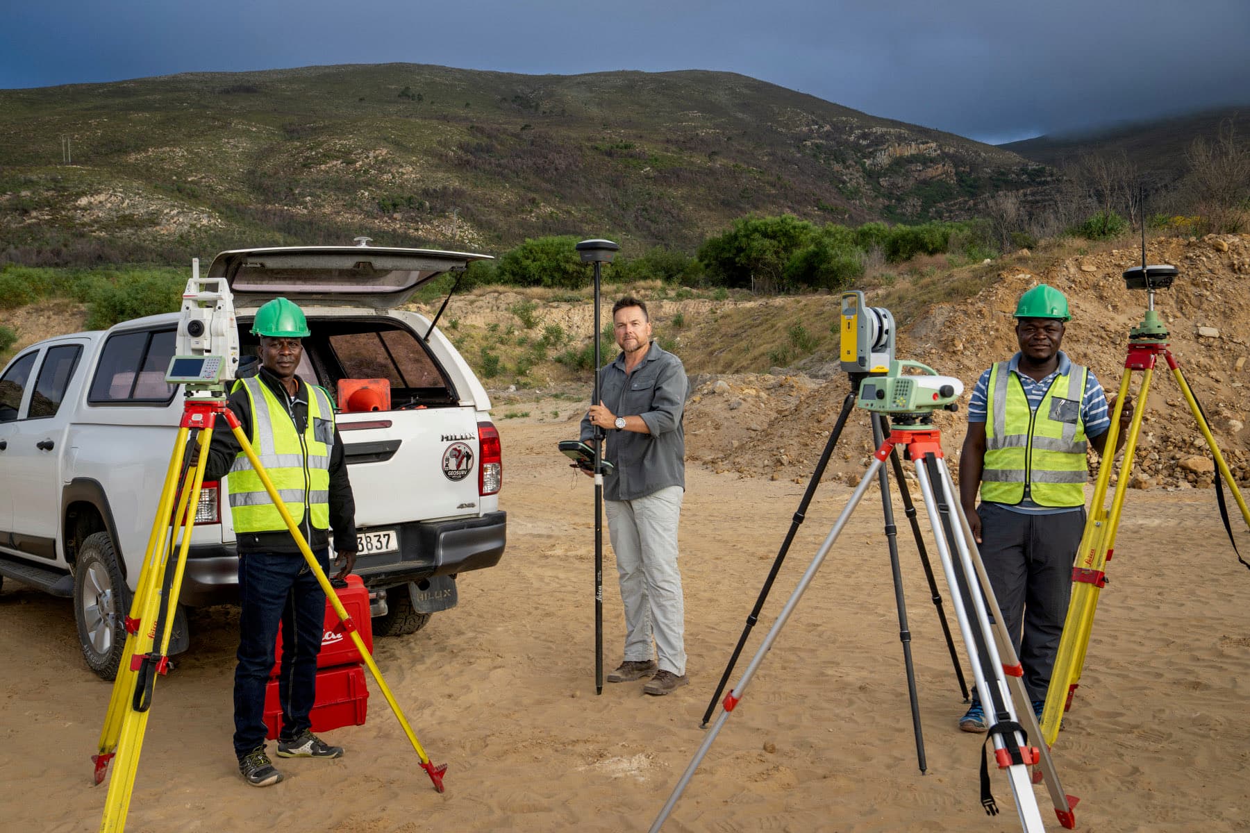 Three GeoSurv surveyors on site with two total stations, GNSS rovers and the branded company bakkie.
